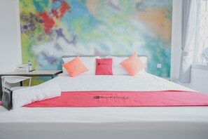 Una habitación de hotel con una cama, una colcha roja y un cuadro abstracto colorido en la pared.