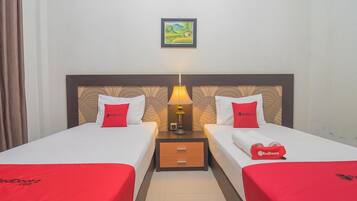 A hotel room with two beds, each with a red bedspread and matching pillows, a nightstand with a lamp, and a framed picture on the wall.