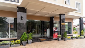 L’entrée d’un hôtel, avec un passage couvert, des plantes en pot et un panneau indiquant la présence d’un restaurant.