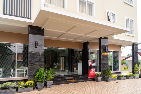 A hotel entrance with a covered walkway, potted plants, and a sign indicating a restaurant.