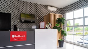Un espace d'accueil avec une enseigne RedDoorz, un téléviseur à écran plat, un comptoir d'accueil en bois et une plante en pot.