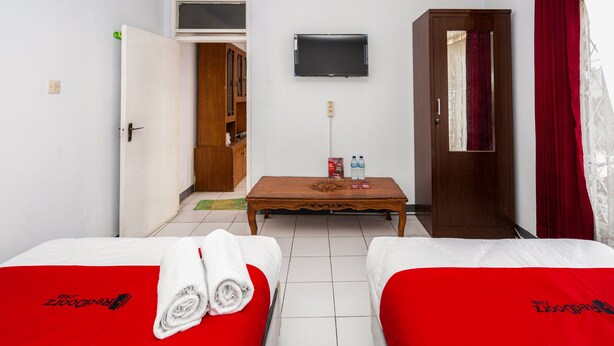 A hotel room with two beds, a TV on the wall, a wooden cabinet, and a table with two water bottles. - RedDoorz Syariah near RSUD Cimacan (Cipanas)
