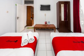 A hotel room with two beds, a TV on the wall, a wooden cabinet, and a table with two water bottles.