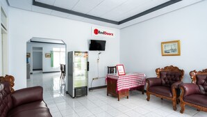 A modern hotel lobby with a reception desk, a refrigerator, a television, and classic leather sofas. - RedDoorz Syariah near RSUD Cimacan (Cipanas)