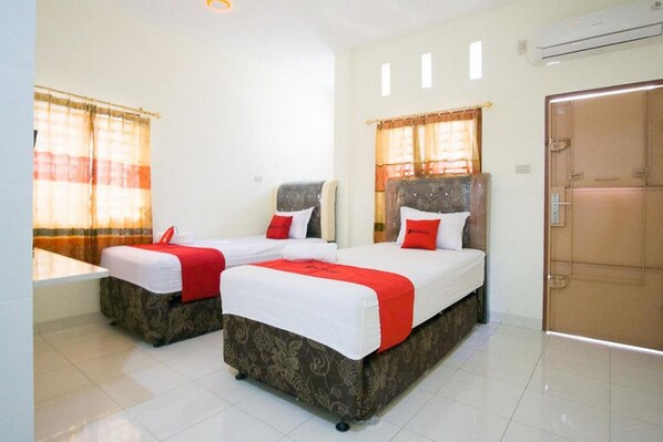 A hotel room with two beds, each with a red and white bedspread, and a large wardrobe. - RedDoorz @ Pematangsiantar 2 (Pematangsiantar)