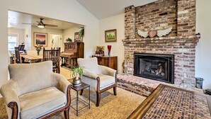 Un salón con chimenea de ladrillo, dos sillones, una mesa de centro y un ventilador de techo.