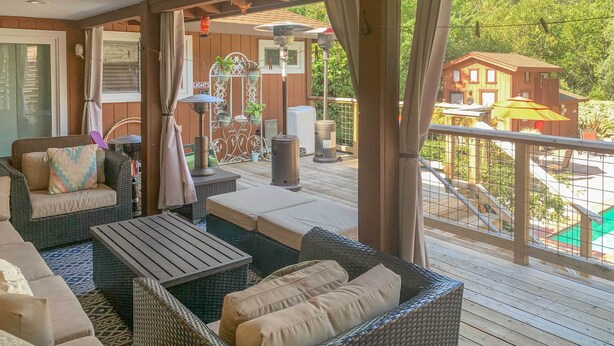 Un espacio de estar al aire libre cubierto con mobiliario de mimbre, una mesa y vistas a una casa y una piscina.