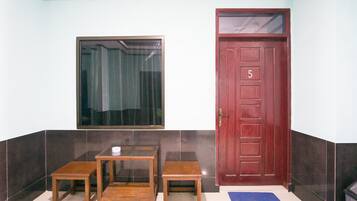 A room with a wooden door marked with the number 5, a window with a curtain, and two small wooden tables.
