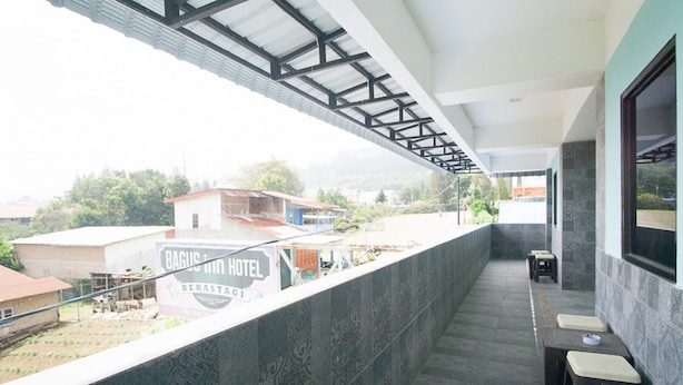 A hotel balcony with a view of the surrounding area, including a sign for 'Baguis Hotel' and a small seating area with stools. - RedDoorz near Mikie Holiday Funland Berastagi (Berastagi)