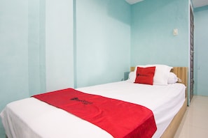 Un llit individual amb una colcha vermella i blanca, un reposacapses de fusta i un coixí vermell amb el text "RedDoorz".
