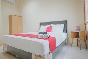 A hotel room with a bed, a wooden wardrobe, and a small wooden side table.
