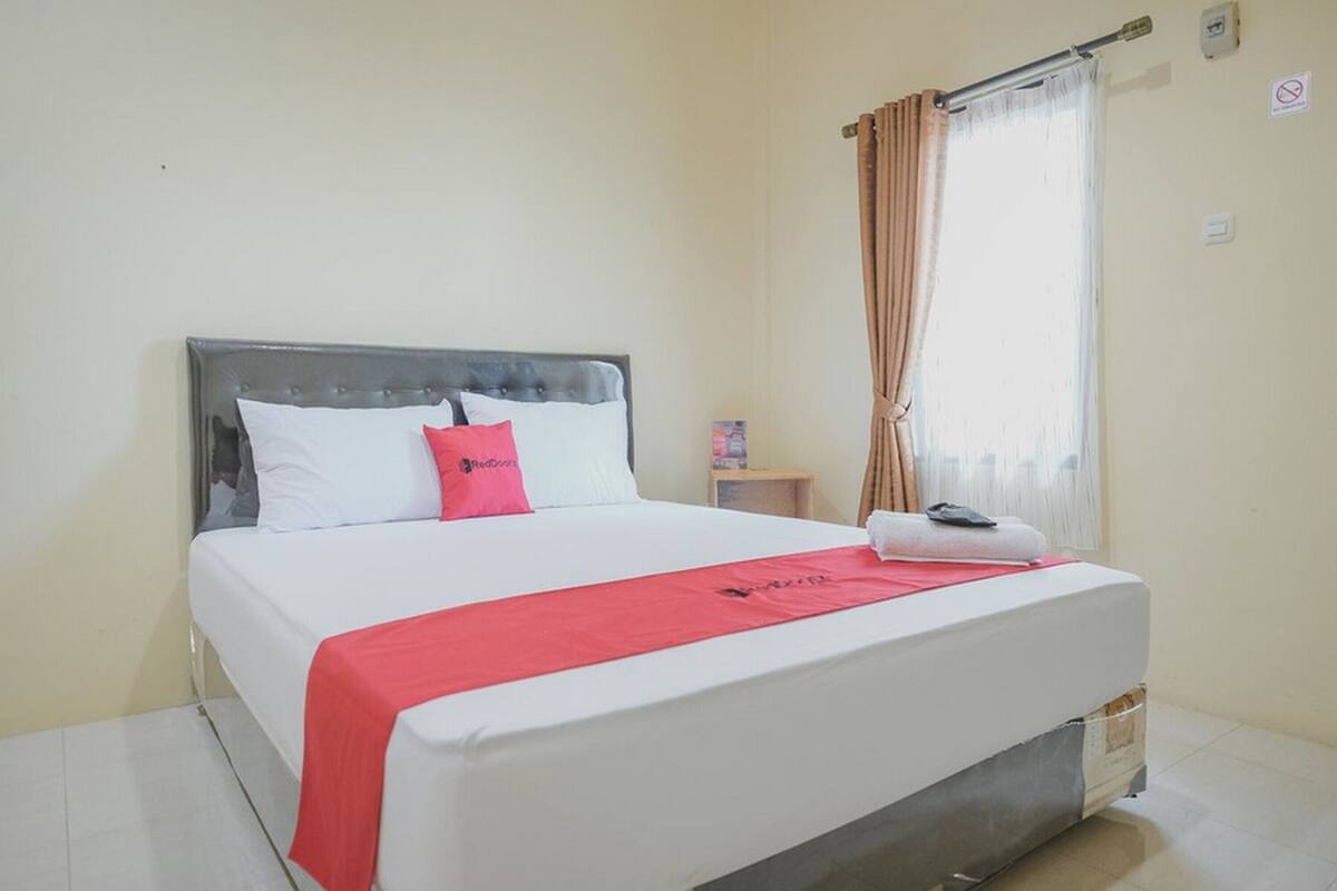 A neatly made bed with white and red bedding, a grey headboard, and a red throw.