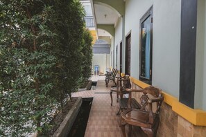 A corridor with wooden benches, a potted plant, and a tiled floor. - RedDoorz Syariah near Tugu Juang Jambi 2 (Jambi)