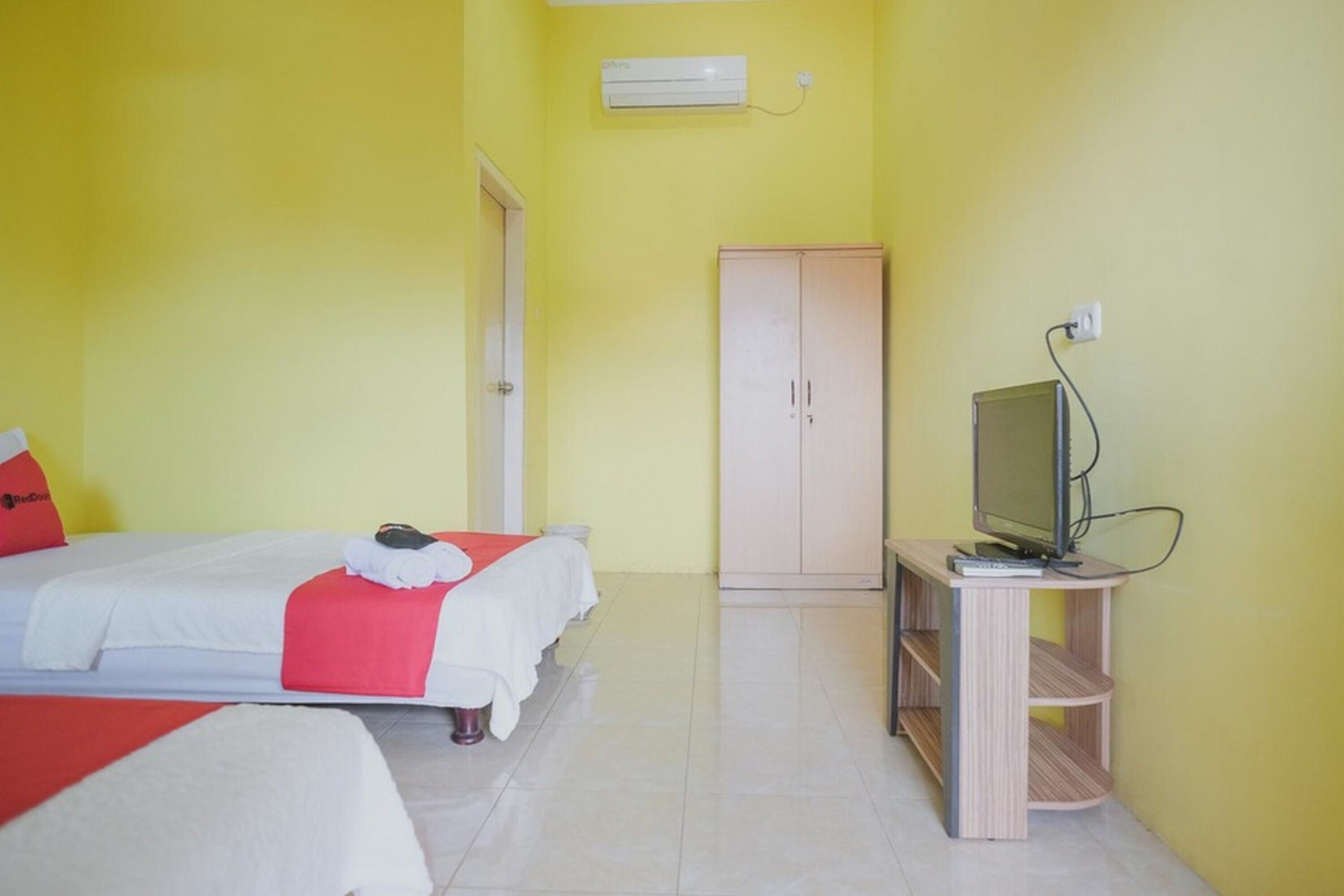 Une chambre d’hôtel avec deux lits, un téléviseur posé sur un meuble en bois et une armoire.