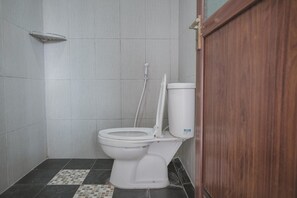 A small, tiled bathroom with a toilet, a shower, and a wooden door. - RedDoorz Syariah near Tugu Juang Jambi 2 (Jambi)