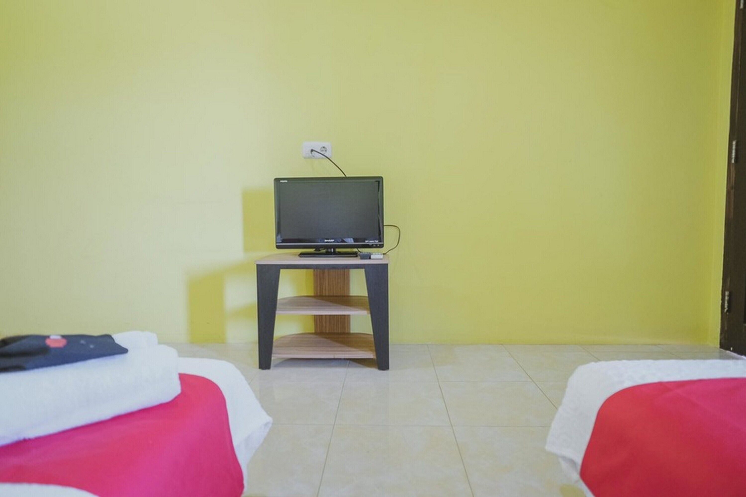 Una habitación con dos camas, un televisor sobre un mueble y una pared amarilla.