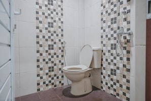 Une salle de bain avec des toilettes, une douche et des murs carrelés.