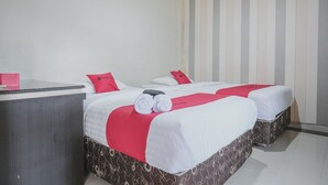 Habitación de hotel con dos camas, cada una con ropa de cama blanca y roja, un escritorio con un objeto rosa y una pared a rayas.