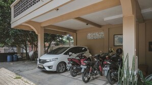 Un área de estacionamiento techada con un SUV blanco y varias motocicletas aparcadas.