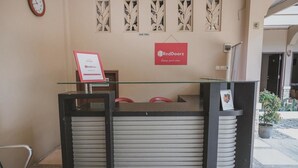 Un mostrador de recepción con cubierta de vidrio, un letrero de RedDoorz y un reloj en la pared.