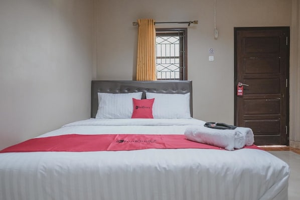 Un lit bien fait, recouvert d’une couverture rouge et blanche, avec un oreiller orné d’un logo et une serviette posée à côté.