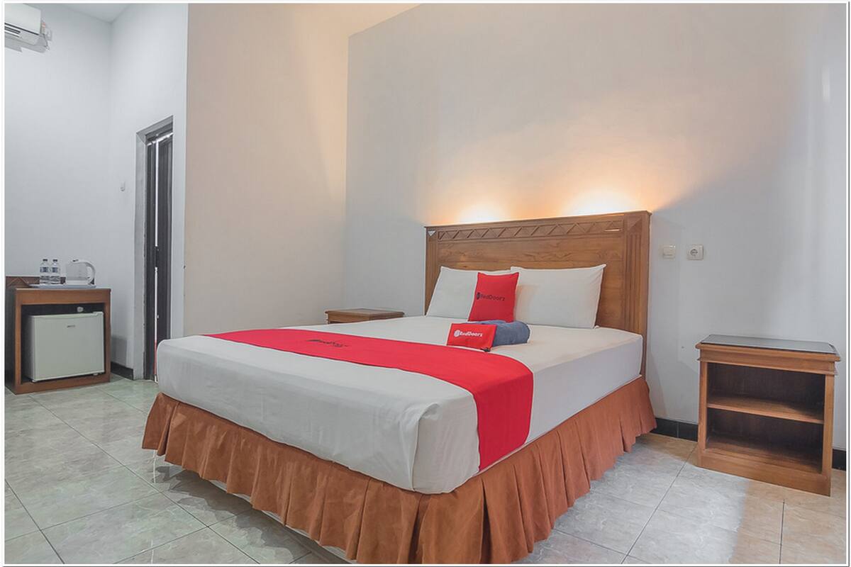 A neatly made bed with a red and white bedspread, a wooden headboard, and a small bedside table with a lamp.