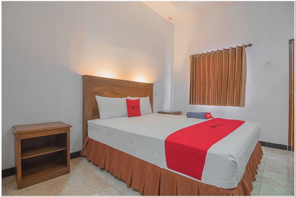A neatly made bed with a wooden headboard, a bedside table, and a window with curtains.