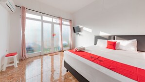 Quarto de hotel com uma cama grande, uma TV fixada na parede e vista para o exterior pela porta de correr de vidro.