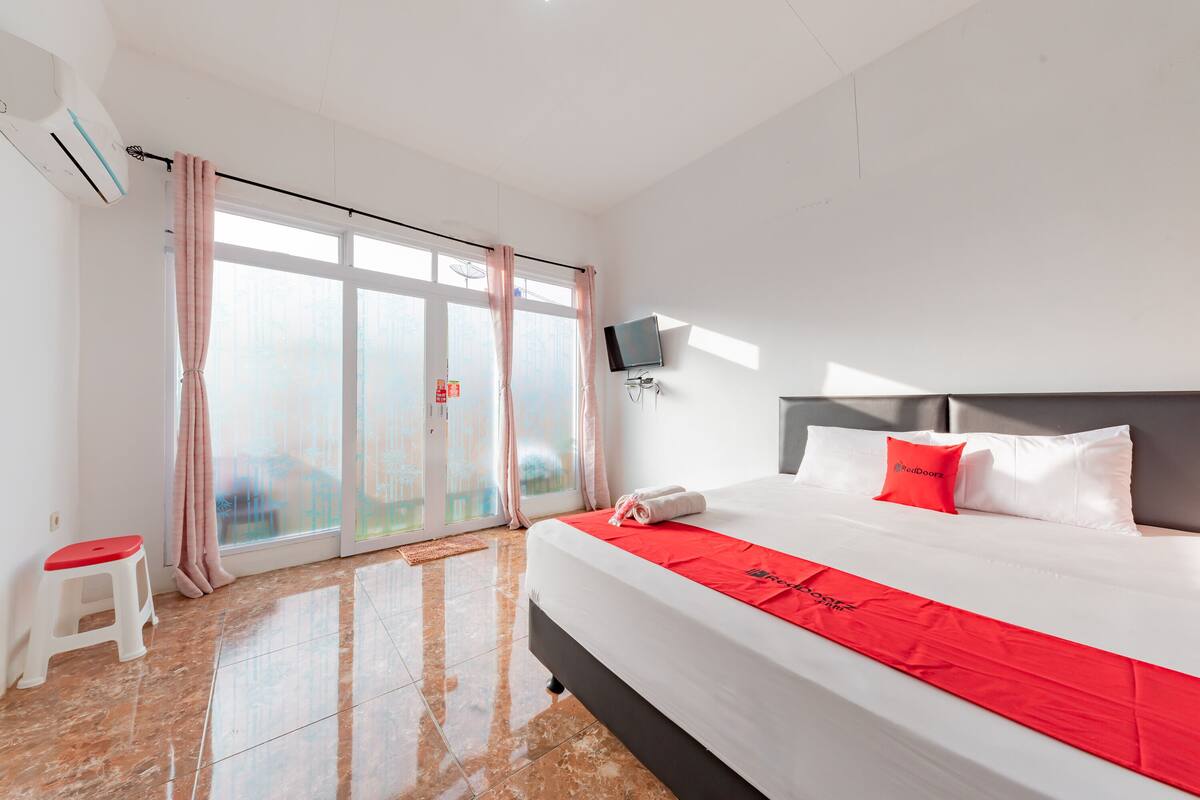 Een hotelkamer met een groot bed, een aan de muur bevestigde televisie en uitzicht op het omliggende landschap door de schuifdeur.