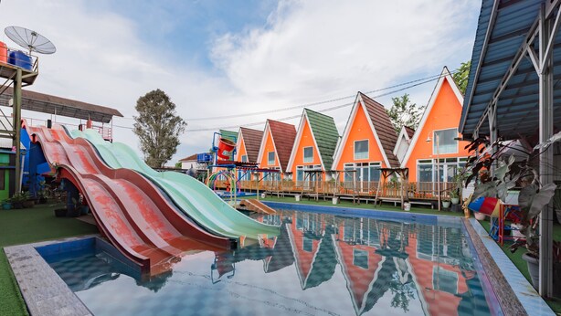 Piscina com toboáguas coloridos, cercada por casas laranja e verdes sob um céu claro.