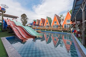 A swimming pool with colorful slides, surrounded by orange and green houses with a clear sky. - Formerly Reddoorz Resort Syariah Jaya Tirta Abadi (Sukamanah)