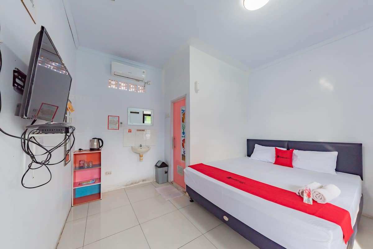 Een hotelkamer met een bed, een televisie, een plank met toiletartikelen en een kleine prullenbak.