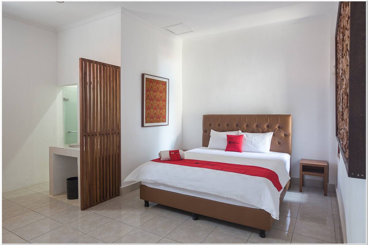 Een hotelkamer met een groot bed, een houten scheidingswand, een klein tafeltje en een ingelijste foto aan de muur.