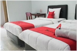 A hotel room with two beds, each with white bedding and red accents. There is a small table with a chair and a bottle of water on it.