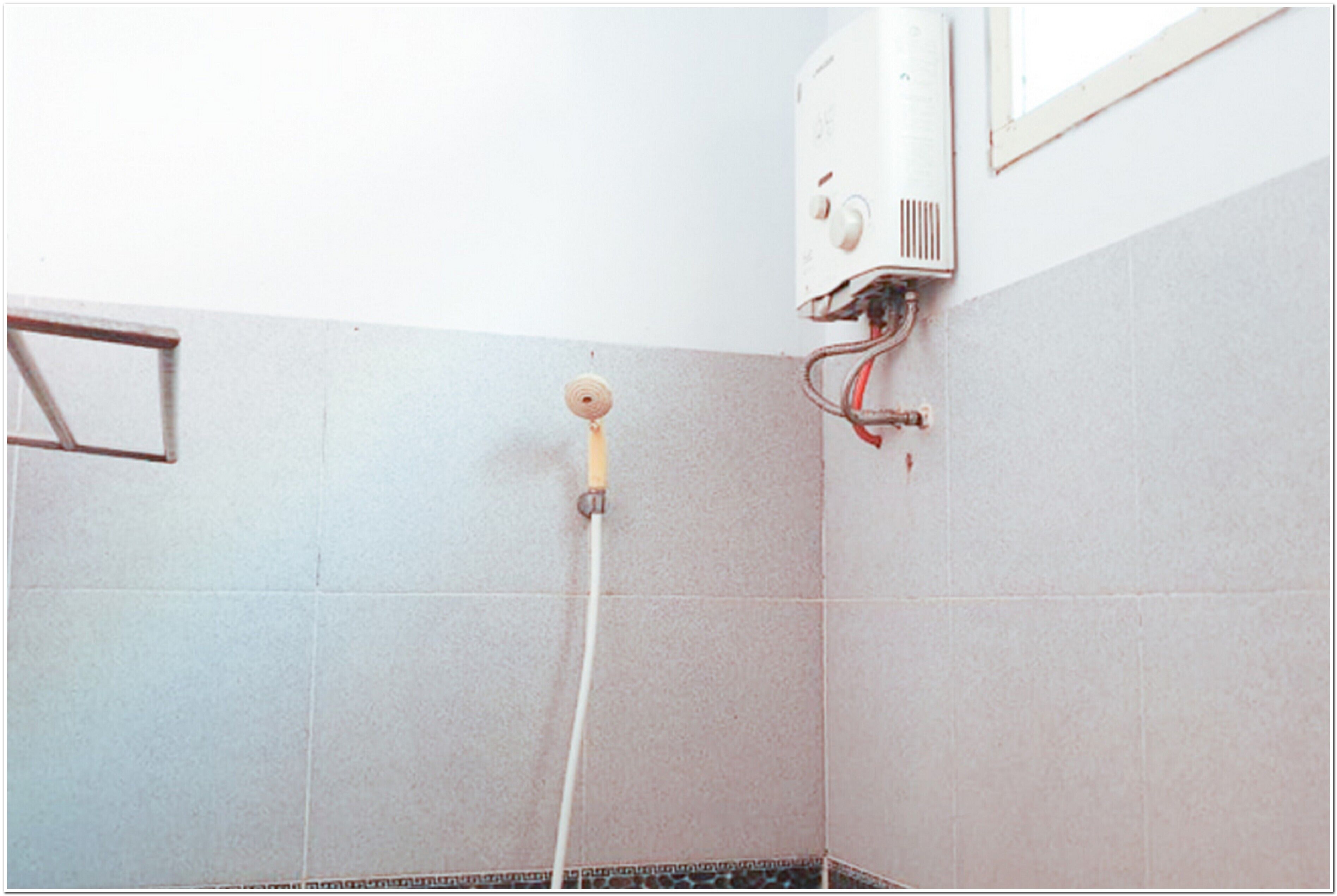 Un baño con ducha, paredes enlosadas y un enchufe a la vista.