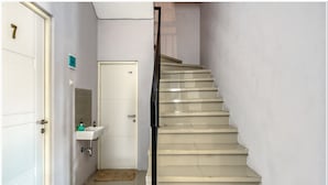 Un escalier avec une rampe, une porte blanche portant un numéro et un petit lavabo avec un miroir.