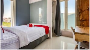 Une chambre d’hôtel moderne, équipée d’un lit, d’un bureau et de grandes fenêtres donnant sur un paysage agréable.