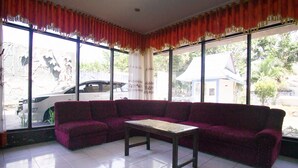 Ein Zimmer mit einem violetten Sofa, einem kleinen Tisch und großen Fenstern mit Vorhängen.