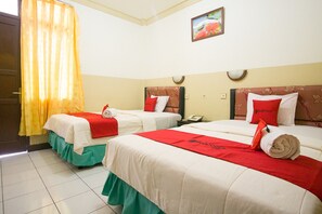 A hotel room with two beds, each with a red blanket and pillow, a small table with a phone, and a painting on the wall.