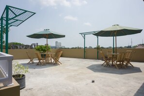 A rooftop terrace with outdoor furniture, umbrellas, and a view of the city skyline. - Reddoorz Syariah Near Taman Pelangi Monjali (Ngaglik)