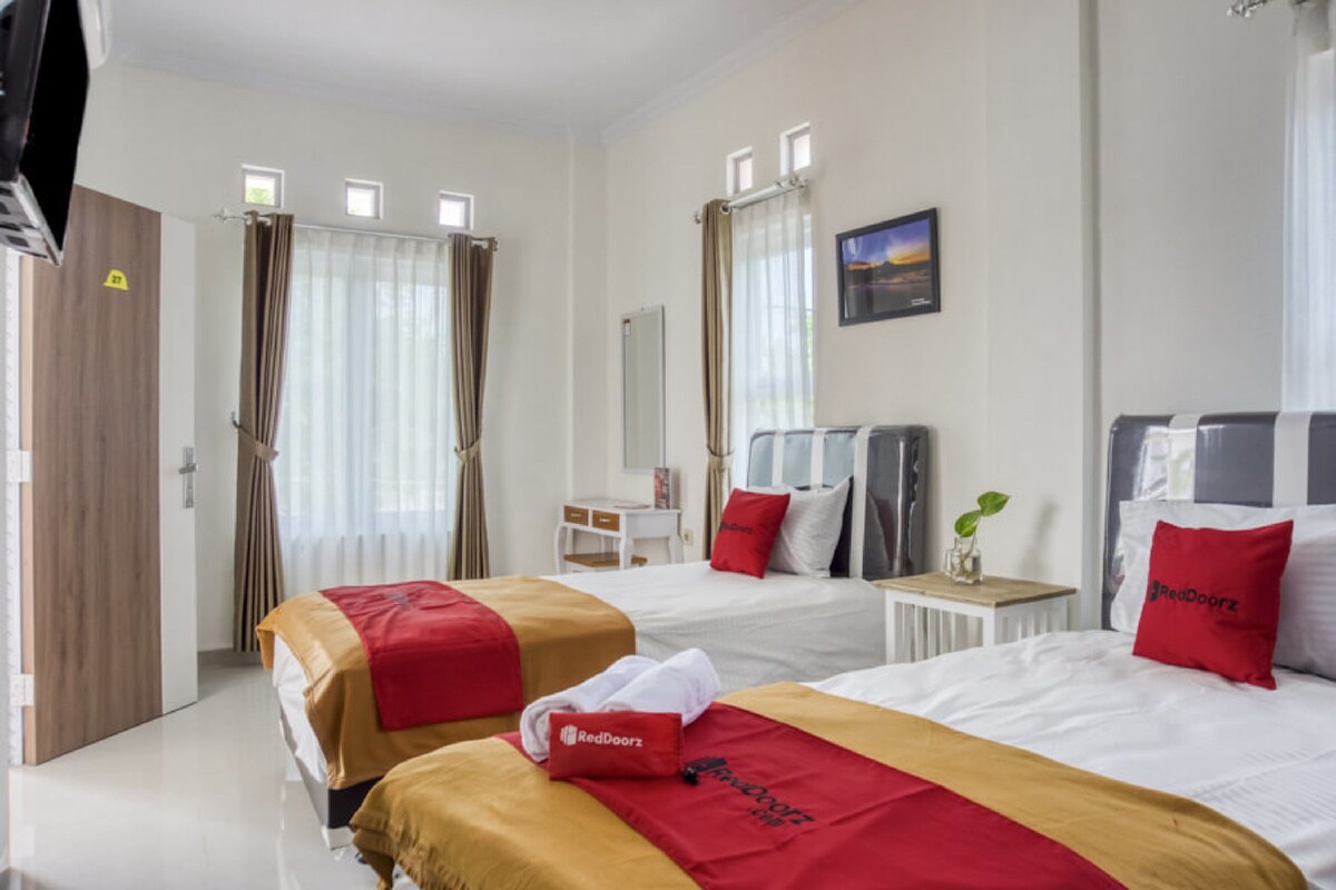 A hotel room with two beds, a desk, a chair, a television, and a window with curtains.