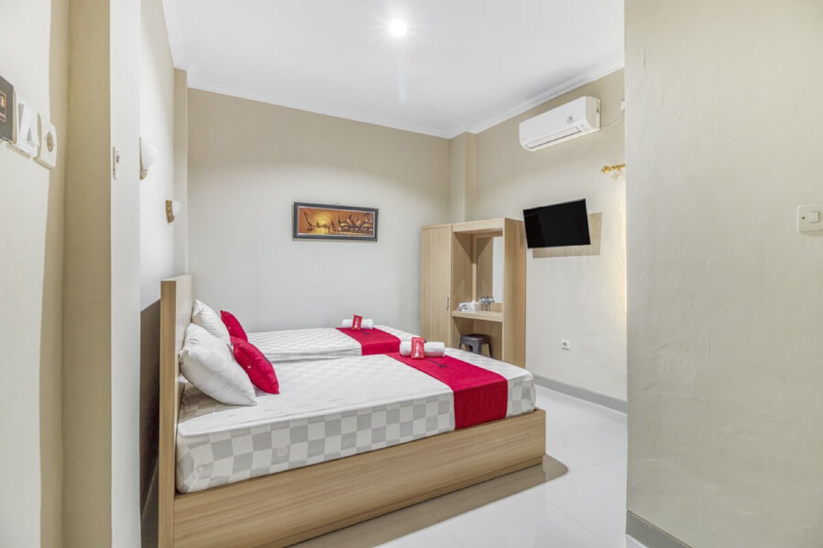 Habitación de hotel con dos camas, un televisor de pantalla plana montado en la pared y un mueble-espejo pequeño.