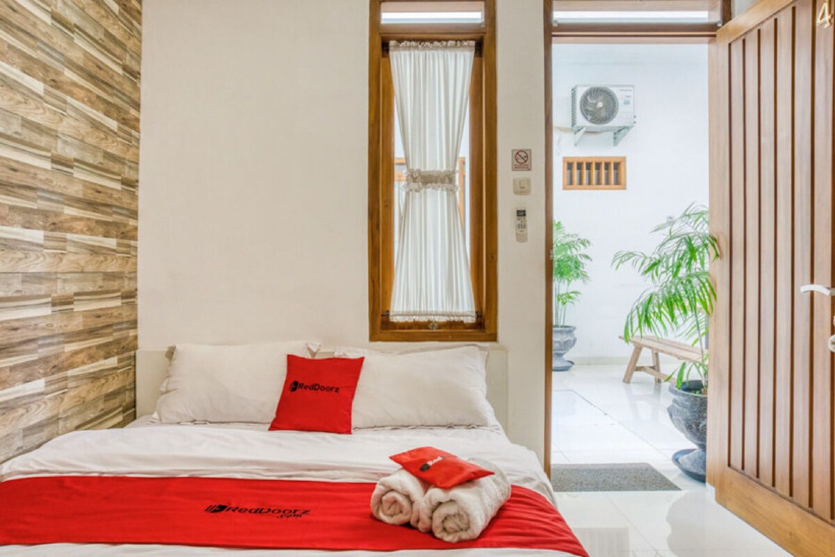 A hotel room with a bed, a red blanket, and a wooden wall.