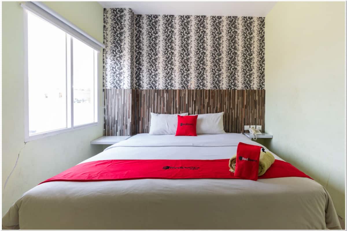A hotel room with a large bed, a window, and a patterned curtain.