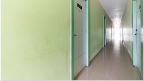 Un pasillo largo y estrecho con paredes y puertas de color verde, que conduce a una habitación luminosa al final.