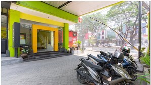Una motocicleta estacionada frente a un edificio con fachada verde y amarilla, un letrero que indica una estación de lavado y un área de acceso pavimentada.