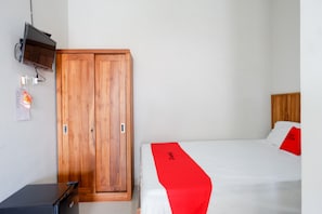 Ein Schlafzimmer mit Holzschrank, Bett mit weißer Bettwäsche und roten Akzenten sowie einem kleinen Schreibtisch.