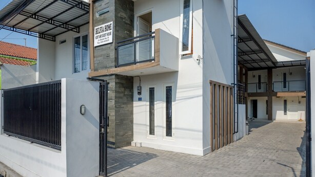 A modern two-story house with a balcony, a gated entrance, and a paved driveway.