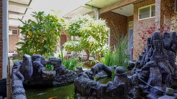A courtyard with a koi pond, stone sculptures, and lush greenery.