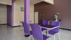 A room with purple chairs and a table, a door, and a wall with a poster. - RedDoorz near RSUD Kebumen (Kebumen)